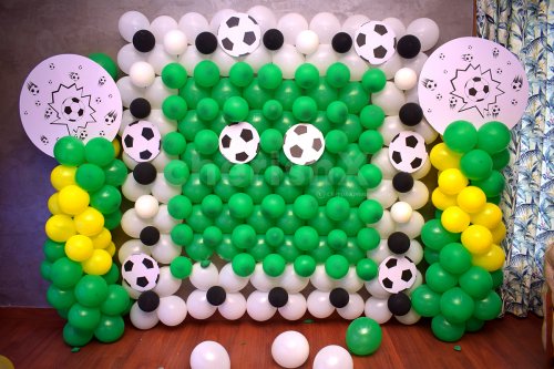 The wall is decorated with bunches of green, white and yellow balloons.