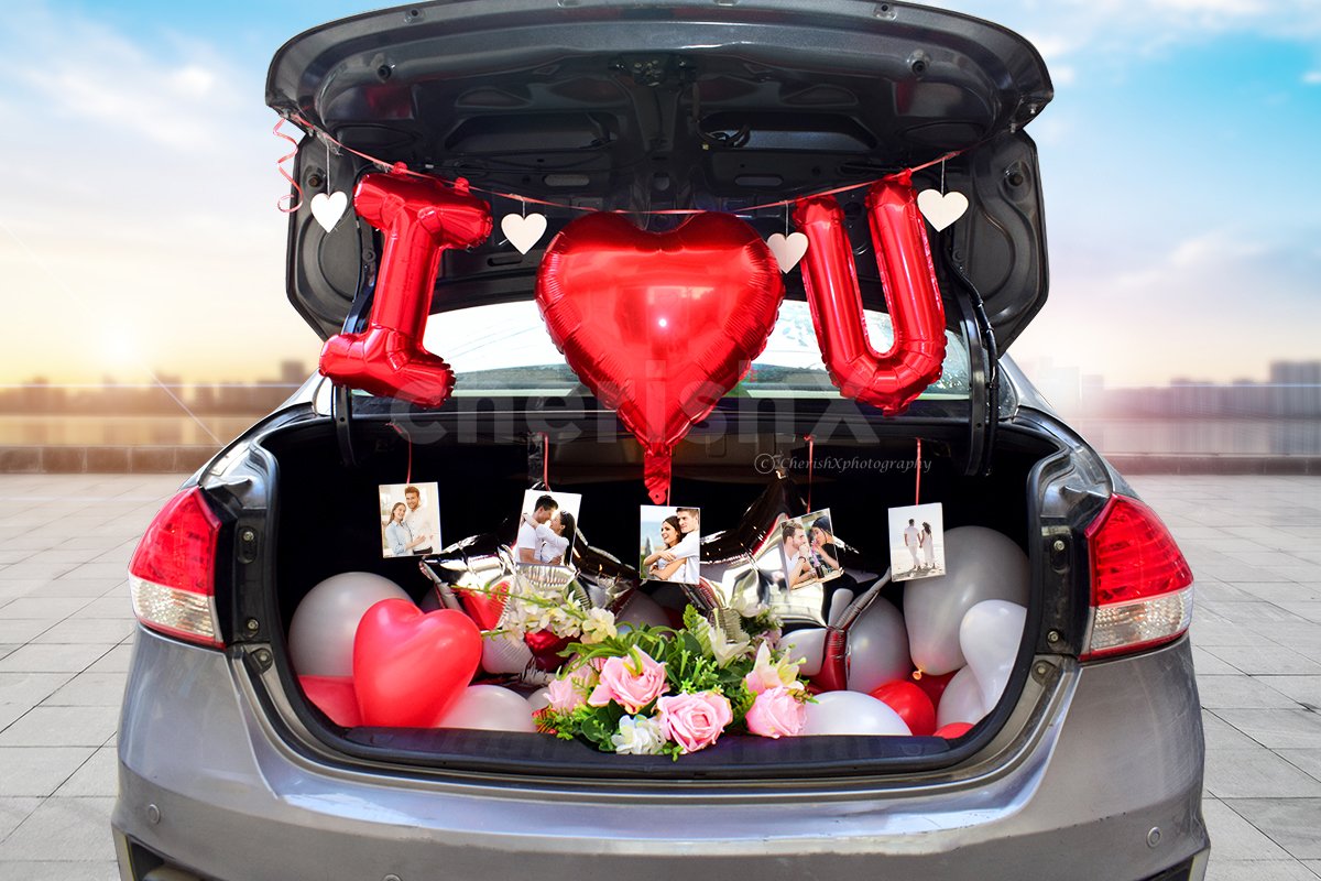 Valentine’s Day Surprise in a car boot featuring I love you foil balloons, flower bouquets, red and white balloons along with hanging photographs. 