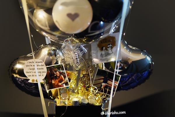The bucket includes silver heart shaped balloons, silver cup shaped chocolates, 2 photos, Rakhi and lumba set with tika and kumkum.